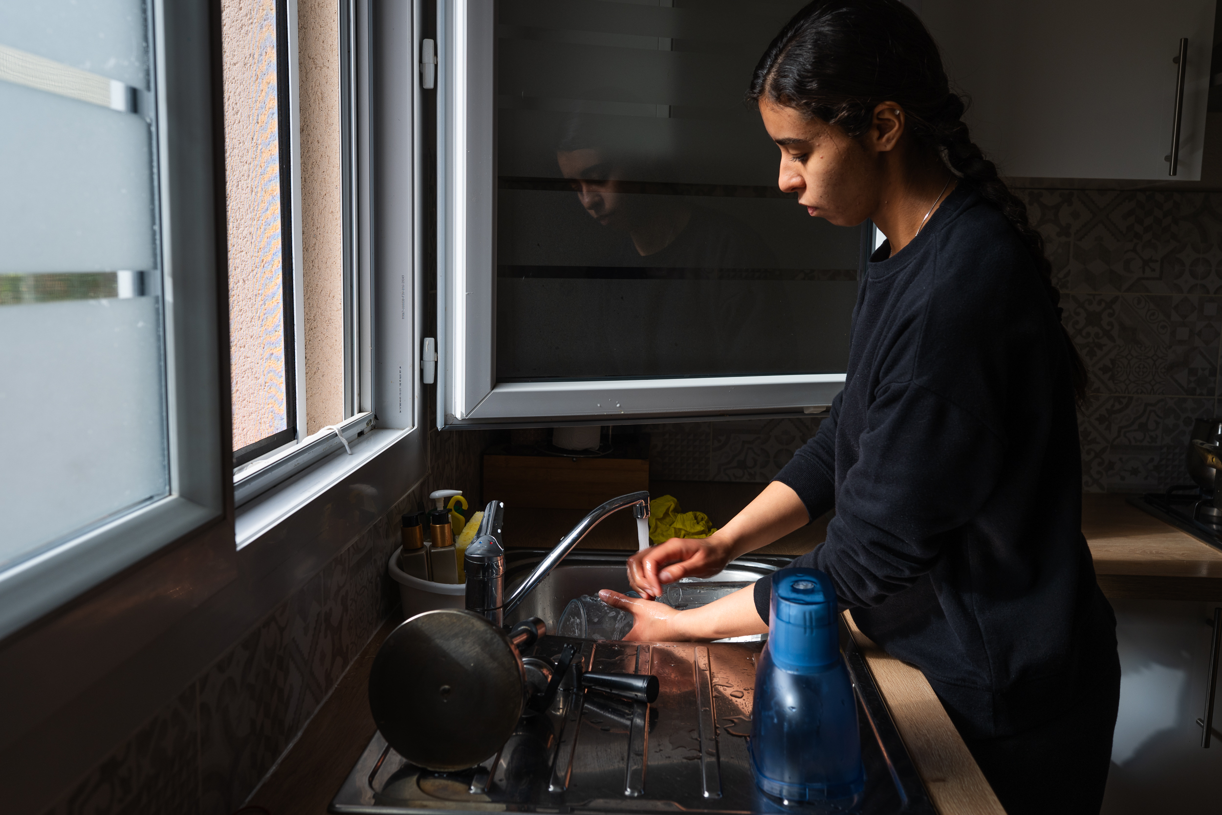 Person washing dishes beside an open window.