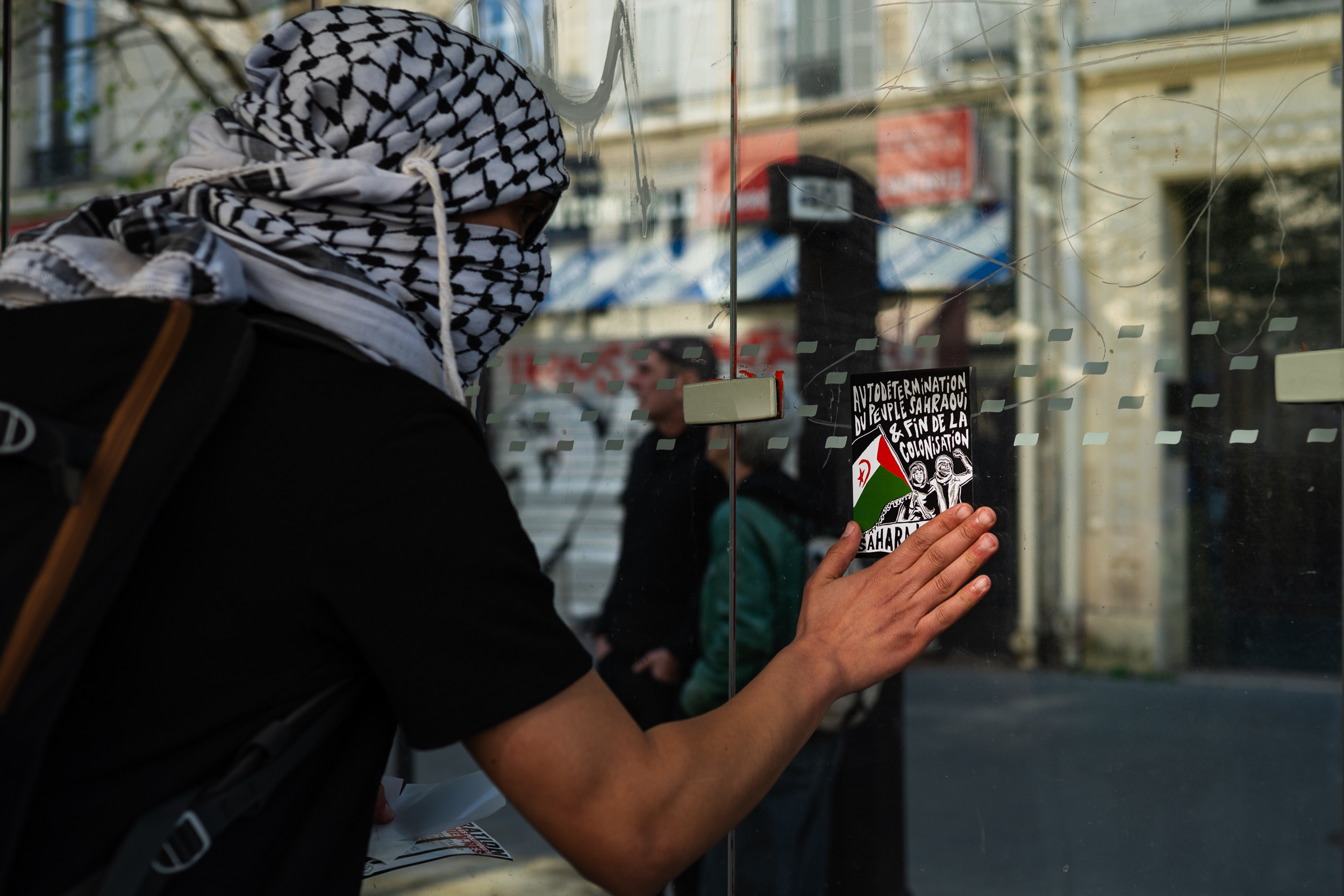 Hand placing a Sahrawi solidarity sticker on glass.