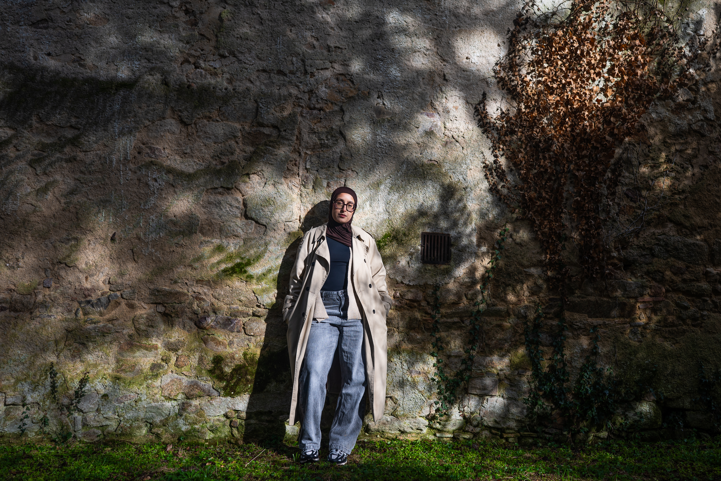 Portrait beside a stone wall in dappled light.