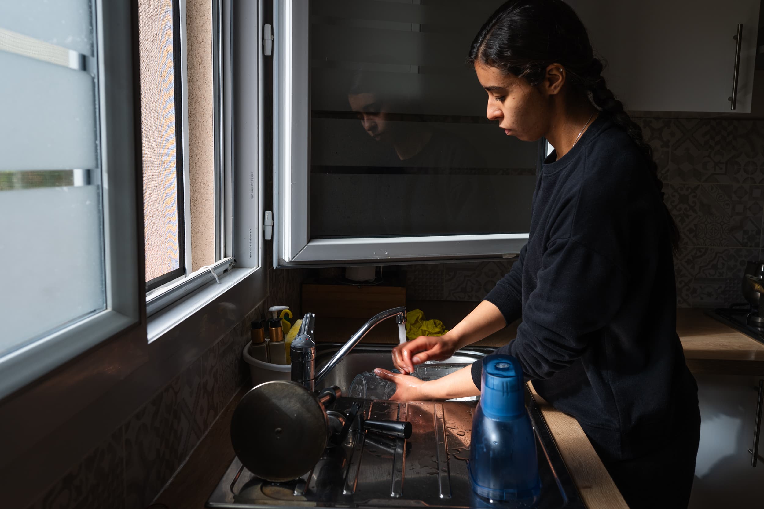 Person washing dishes beside an open window.